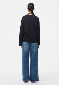 Μαύρο μακρυμάνικο πουκάμισο και φαρδιές μπλε τζιν παντελόνες. Πλέκτο υλικό στο πουκάμισο, ξεθωριασμένο φινίρισμα στις τζιν παντελόνες, με ορατές ραφές και τσέπες.