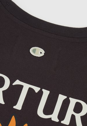 T-shirt in cotone nero con un grande testo stampato bianco e un design floreale arancione, con un piccolo logo ricamato vicino al collo.