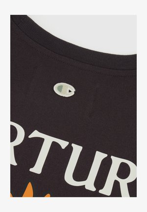 T-shirt in cotone nero con un grande testo stampato bianco e un design floreale arancione, con un piccolo logo ricamato vicino al collo.