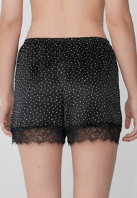 Zwarte satijnen shorts met witte stippen, een elastische tailleband en een delicate marineblauwe kantafwerking aan de zoom. Over het geheel een gladde textuur.