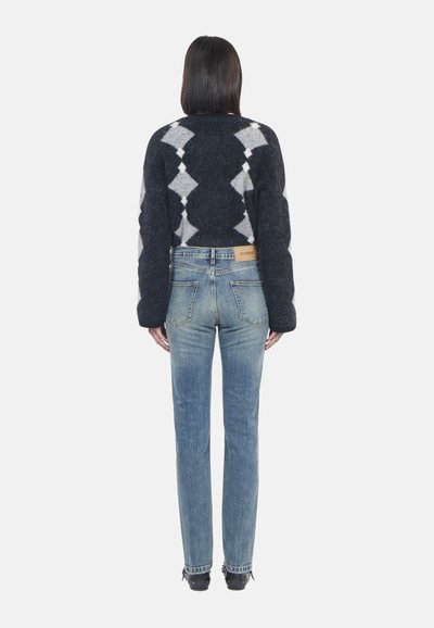 Maglione lavorato a maglia in un blu navy scuro con motivo a diamante, abbinato a jeans dritti blu sbiaditi. Presenta un'etichetta sulla vita e scarpe nere.