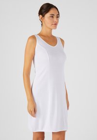 Robe sans manches blanche avec un décolleté en V, fabriquée en tissu lisse, présentant des coutures latérales courbées et une longueur au genou.
