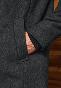 Šedý kabát ze směsi vlny s herringbone vzorem, má boční kapsu a detail žebrovaného manžetu. Jemná textura a přizpůsobený design.