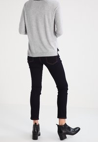 Jersey de manga larga gris claro, con aberturas laterales, combinado con jeans ajustados oscuros y botines negros con acabado texturizado.