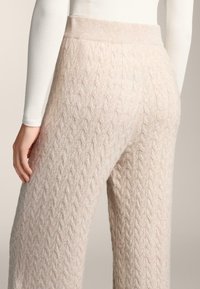 Pletené široké nohavice v jemnej béžovej farbe, s káblovým vzorom, rebrovaným pásom a textúrou na povrchu. Bez viditeľných kovových doplnkov alebo akcentov.