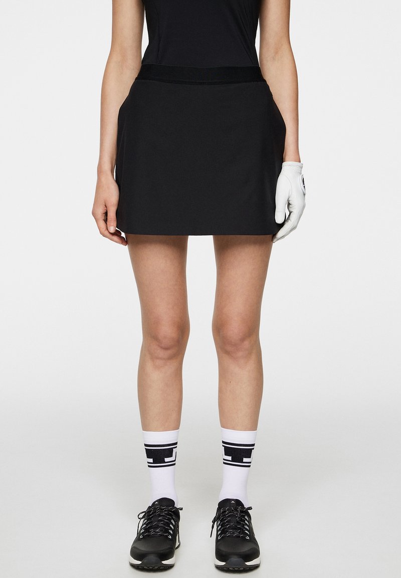 Svart golfsort med en mjuk textur och en bred midjeband, som kombineras med svarta sneakers och vita strumpor med en svart grafisk design.