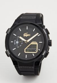 Digital watch with a black rubber strap and textured dial. Features gold accents, analog hands, and a digital display showing time and date.