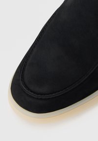 Sorte semsket sko med avrundet tå, aksentert søm og en gjennomsiktig gummisåle. Glatt tekstur, minimalistisk design.