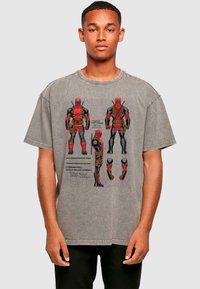 Gray oversized t-shirt featuring a graphic design of a character in red and black with text elements, round neck, and short sleeves.