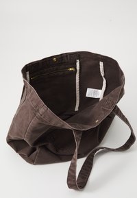 Brown canvas tote bag with a top opening, interior zipper pocket, and two additional slip pockets. Features stitching and gold-tone hardware.