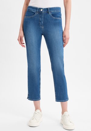 Helle blaue, knöchellange Jeans mit fünf Taschen, Knopfverschluss und fransigem Saumdetail. Kombiniert mit weißen Sneakers.