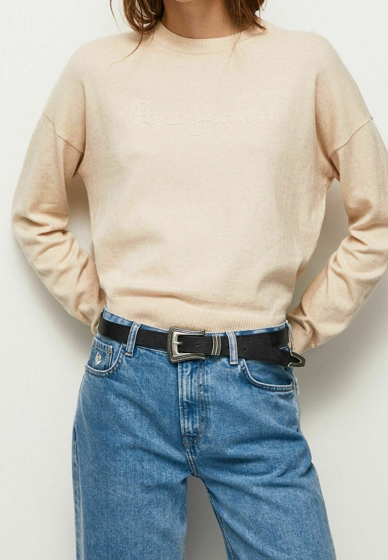 Jasno beżowy sweter z dzianiny z prążkowanymi mankietami i dołem, z haftowanym logo "Pepe Jeans". W zestawie z jasnoniebieskimi dżinsami z wysokim stanem i czarnym paskiem.