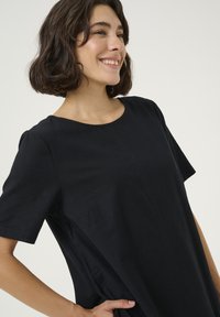 Schwarzes Kurzarmkleid mit rundem Ausschnitt, das ein einfaches Design und subtile Nähte aufweist. Glatte Textur, knielanger Schnitt.