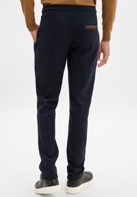 Granatowe dresy z elastycznym pasem, bocznymi kieszeniami i kontrastowym brązowym skórzanym akcentem na tylnej kieszeni. Miękka, teksturowana tkanina.