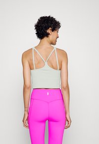 Sutia desportivo cinza claro com um design de costas nadador, combinado com leggings rosas de cintura alta que apresentam bolsos laterais e sutis detalhes de costura.