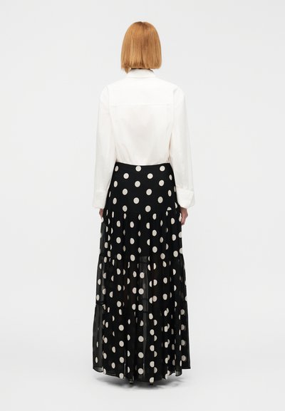 Λευκό πουκάμισο με γιακά συνδυασμένο με μαύρη, στρωματοποιημένη μακριά φούστα με μεγάλα λευκά πουά. Διαφανές ύφασμα με ρέουσα σχεδίαση.