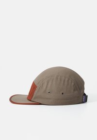 Brown and rust five-panel cap with flat brim, metal ventilation eyelets on side, and Patagonia logo tag on adjustable back strap.