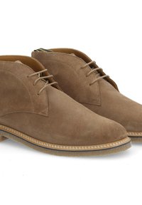 Chaussures en suede marron avec une texture lisse, présentant une forme arrondie, un laçage et un bord contrastant cousu le long de la semelle.