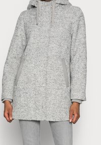 Szary płaszcz o jodełkowym wzorze z kapturem, miękkiej teksturze oraz szarymi akcentami na kieszeniach i mankietach. Prosty krój, długość do połowy uda.