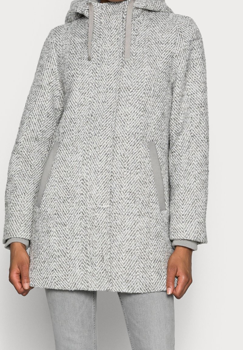 Szary płaszcz o jodełkowym wzorze z kapturem, miękkiej teksturze oraz szarymi akcentami na kieszeniach i mankietach. Prosty krój, długość do połowy uda.