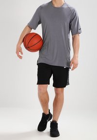 Camiseta deportiva gris de manga corta, combinada con pantalones cortos negros y usada con zapatillas negras mientras sostiene una pelota de baloncesto naranja.