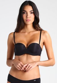 Black padded bra with underwire, adjustable straps, smooth fabric, and a small gold accent in the center. Minimalistic design.