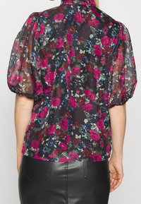 Blusa nera trasparente con maniche a sbuffo, caratterizzata da una stampa floreale colorata nei toni del rosa, verde e blu. Tessuto morbido e scollatura rotonda.
