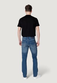 Camiseta negra de cuello redondo, vaqueros de mezclilla azul con cinco bolsillos, ajuste recto y zapatillas blancas. Diseño simple sin patrones visibles.