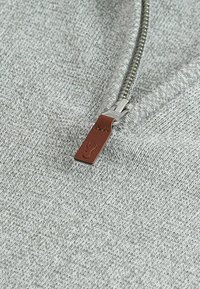 Grau gestrickter Pullover mit einem silbernen Reißverschluss und einem braunen Ledergriff mit geprägten Details. Glatte Textur mit feiner Naht.