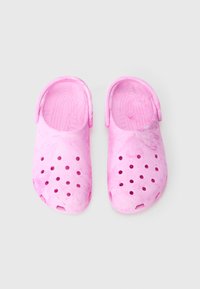 Une paire de sabots roses usés à enfiler, avec des trous de ventilation et des sangles de talon réglables, présentée de dessus sur un fond blanc.