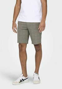 Shorts à carreaux marron clair avec une coupe ajustée, associés à des baskets blanches. Le tissu a une texture tissée et un design structuré.