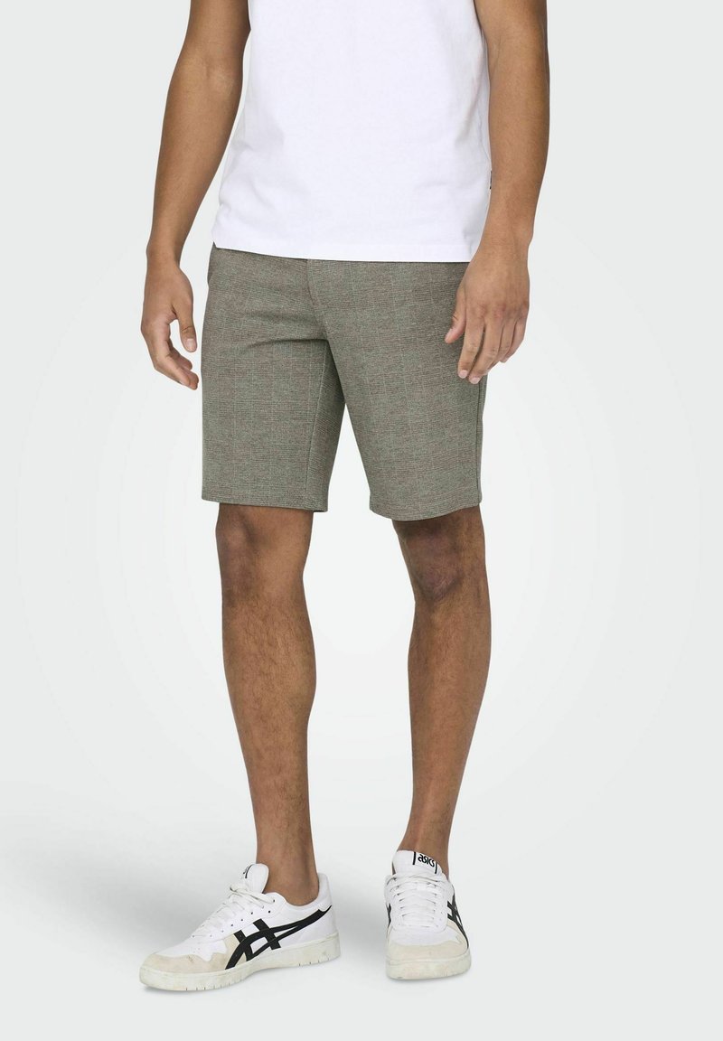 Shorts à carreaux marron clair avec une coupe ajustée, associés à des baskets blanches. Le tissu a une texture tissée et un design structuré.