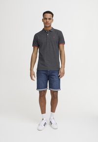 Mørkegrå polo med rød trim, korte ærmer; parret med oprullede denimshorts og hvide sneakers med sorte striber.
