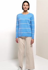 Blauer gestreifter Pullover aus strukturiertem Stoff mit weißen horizontalen Streifen, kombiniert mit cremefarbenen, weit geschnittenen Hosen und weißen Turnschuhen.