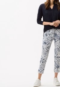 Haut à manches longues bleu marine avec col en V et poche ; pantalon clair à motif floral ; baskets blanches ; tenue décontractée.