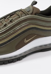 Olivově zelené tenisky Nike Air Max 97 s horní částí z textilu a syntetického materiálu, kovovými akcenty, viditelným vzduchovým polstrováním a strukturovanou podešví.