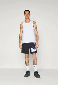 White sleeveless tank top with round neck, paired with dark shorts featuring white lightning pattern. Black athletic shoes and white socks.