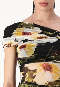 Kukkakuvioinen mekko, jossa on läpikuultavaa mustaa kangasta, jossa on keltaisia ja punaisia kukkia, rypytetty ja olkaimeton muotoilu, sileä pinta ja tiivis siluetti.