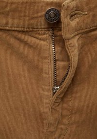 Pantalon en velours côtelé marron avec fermeture éclair en métal, tissu texturé à côtes et un bouton avec un logo en relief à la taille.