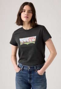 Svart bomull t-skjorte med en fargerik Levi's grafisk logo på forsiden. Paret med blå denim jeans, som viser en klassisk passform og design.