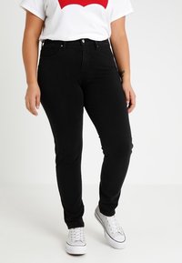 Pantalones vaqueros negros ajustados, de denim, con cintura a media altura y diseño de cinco bolsillos, combinados con una camiseta blanca y zapatillas blancas.