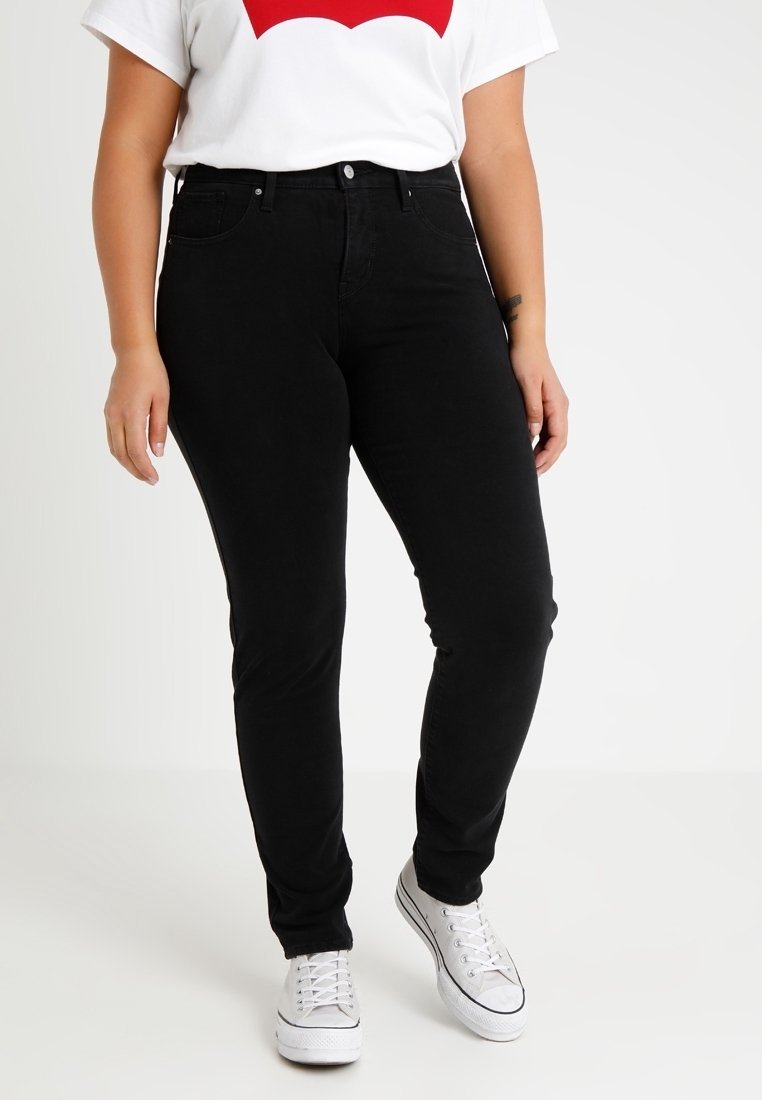 Pantalones vaqueros negros ajustados, de denim, con cintura a media altura y diseño de cinco bolsillos, combinados con una camiseta blanca y zapatillas blancas.