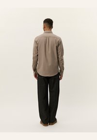 Beige overhemd met lange mouwen, voorzien van een rechte rugnaad en een relaxte pasvorm, gecombineerd met donkere wijde broek.
