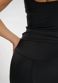 Top a manica lunga attivo nero con silhouette aderente. Presenta un logo ricamato e un design senza cuciture. Realizzato in materiale elastico e traspirante.