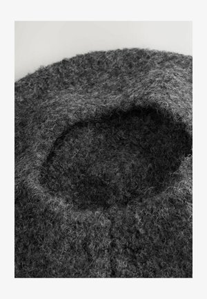 Gekrulde, gestructureerde donkergrijze wollen baret met fuzzy, lusvormige vezels tegen een lichte achtergrond.