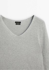 Light grey cotton sweater with a V-neck design. Soft texture and a knitted finish, featuring tags for brand and material information.