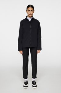 Svart zip-up jacka med hög krage, långa ärmar och avslappnad passform. Bärs över figurnära svarta byxor och svart-vita sneakers.