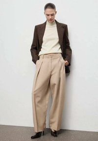 Brauner maßgeschneiderter Blazer, cremefarbener Rollkragenpullover und beigefarbene weit geschnittene Hose. Schwarze High Heels. Glatte Texturen und minimalistisches Design.