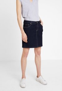 Tmavě modrá džínová sukně s přiléhavým střihem, předními kapsami a kontrastním prošíváním. Nosit s světle šedým topem a bílými teniskami.