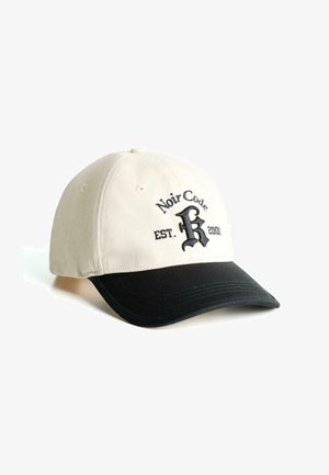 Cappellino da baseball con una corona in cotone beige e visiera nera. Presenta testo ricamato in nero: "Noir Code EST. 2001" con una lettera "R" grafica.